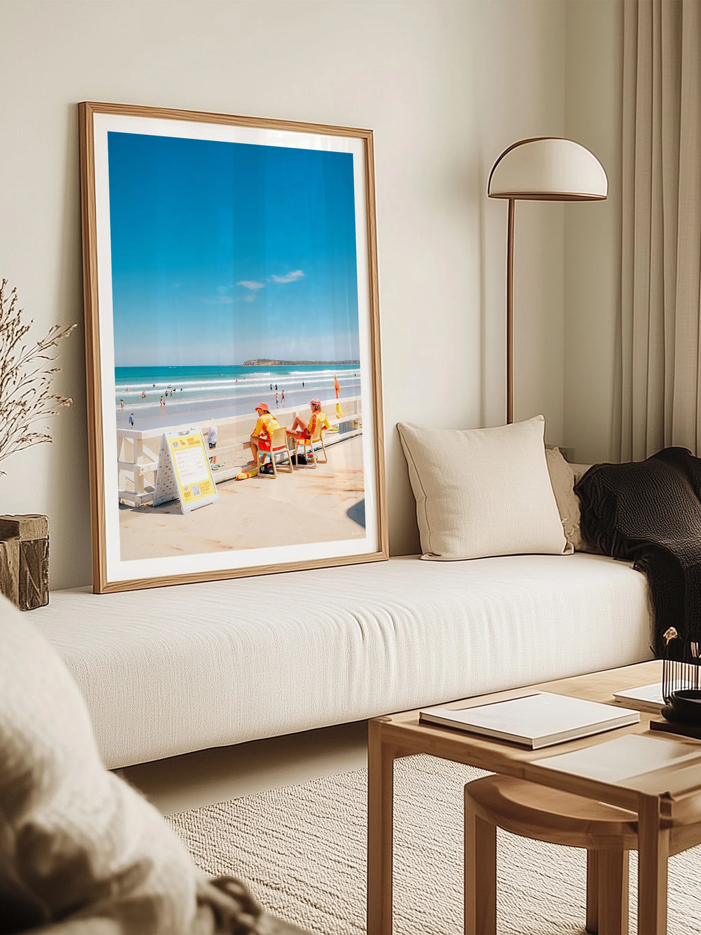 Ocean Grove Surf Life Savers in Summer framed print leaning against a wall behind a cream sofa